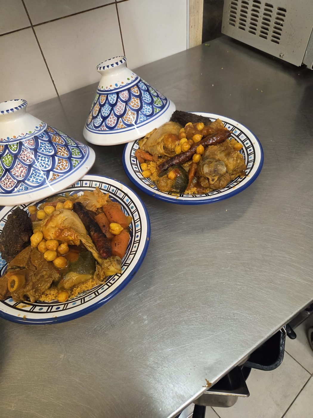 Deux couscous royaux servis dans des plats en céramique tunisienne, avec merguez, poulet, agneau, pois chiches et légumes